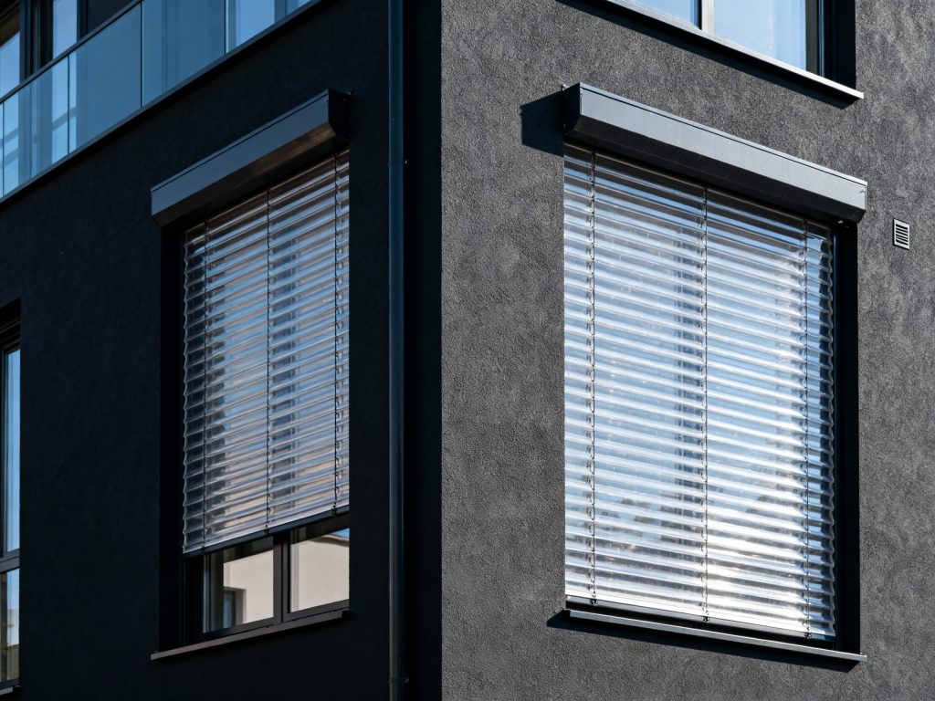 Nowoczesne okno z zamontowanymi żaluzjami zewnętrznymi. Te aluminiowe lamele są częścią systemu zarządzania osłonami okiennymi, który może być kontrolowany za pomocą technologii smart home.