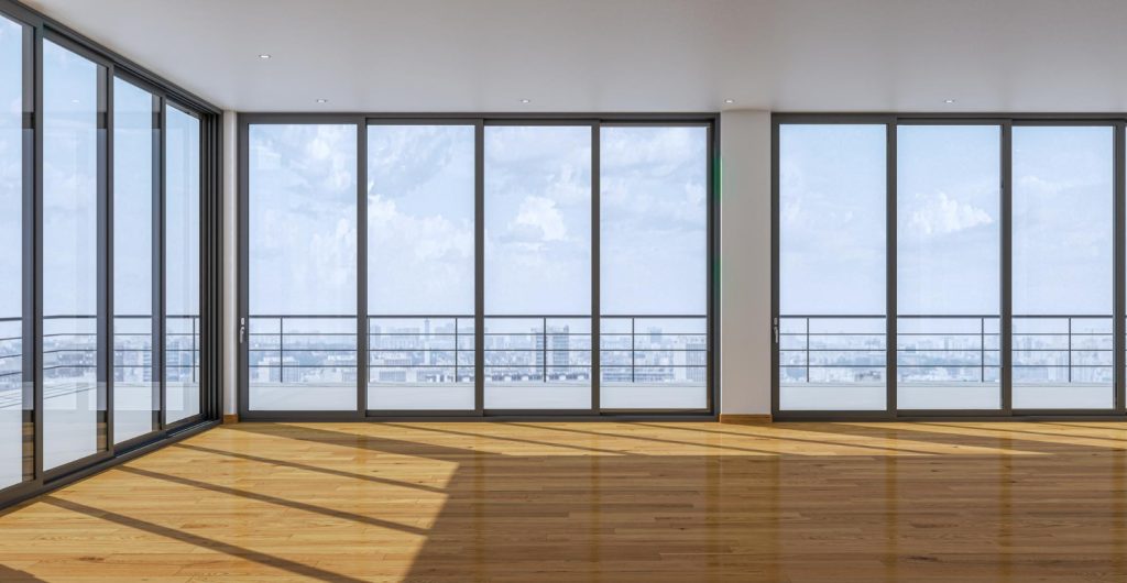 Puste, jasne wnętrze z drewnianą podłogą i dużymi przeszkleniami od podłogi do sufitu, z widokiem na miasto.